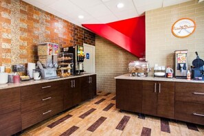 Un coin cuisine avec un mur en briques, un mur d’accent rouge et une horloge sur laquelle est inscrit « Rise & Dine ».