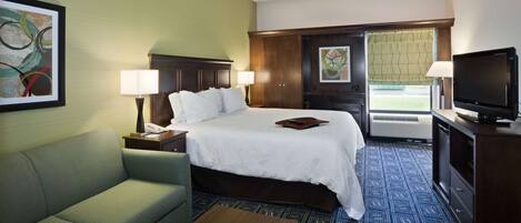 A hotel room with a bed, a sofa, a TV, and a desk with a lamp.