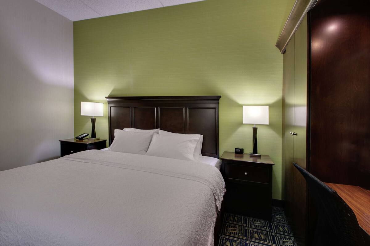 A neatly made bed with white linens, two bedside tables with lamps, and a dark wooden headboard.