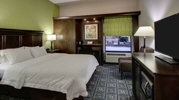 A hotel room with a large bed, a desk with a chair, a television, and a window with blinds.