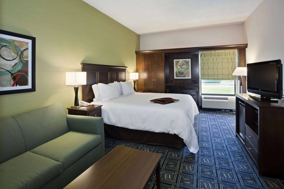 A hotel room with a bed, a green sofa, a TV, and a desk with a lamp.