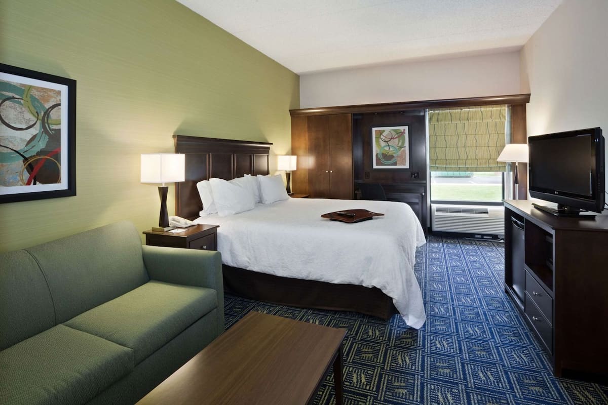 A hotel room with a bed, a green sofa, a TV, and a desk with a lamp.