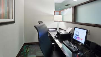 A hotel room with a desk, computer, chair, and a window with blinds.
