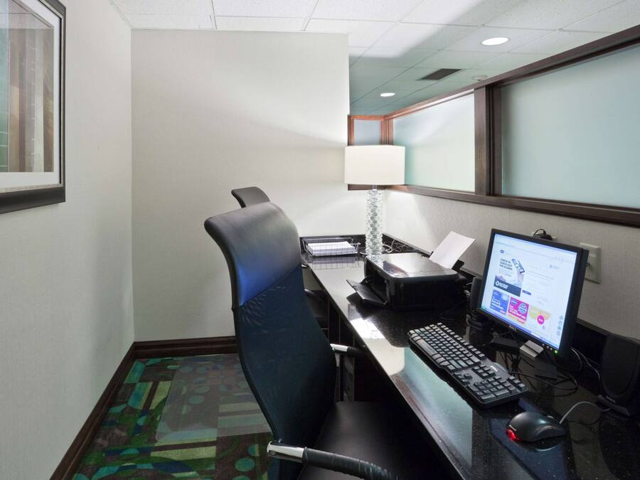 A hotel room with a desk, computer, chair, and a window with blinds.
