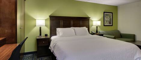 A hotel room with a large bed, two bedside tables with lamps, a green wall, a framed picture, and a patterned carpet.