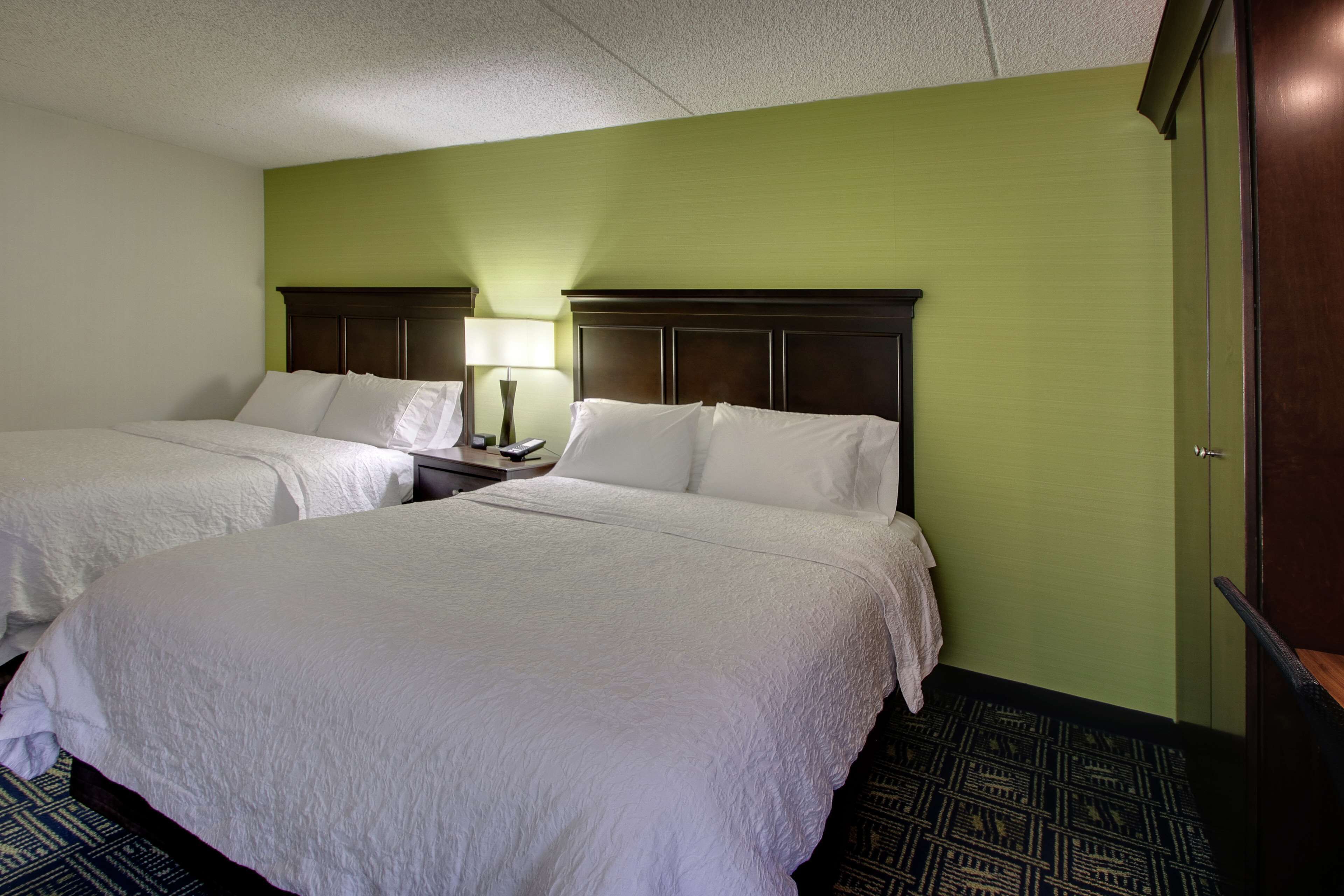 Una habitación de hotel con dos camas, una mesita de noche con lámpara y una pared verde.