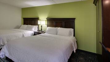 A hotel room with two beds, a nightstand with a lamp, and a green wall.