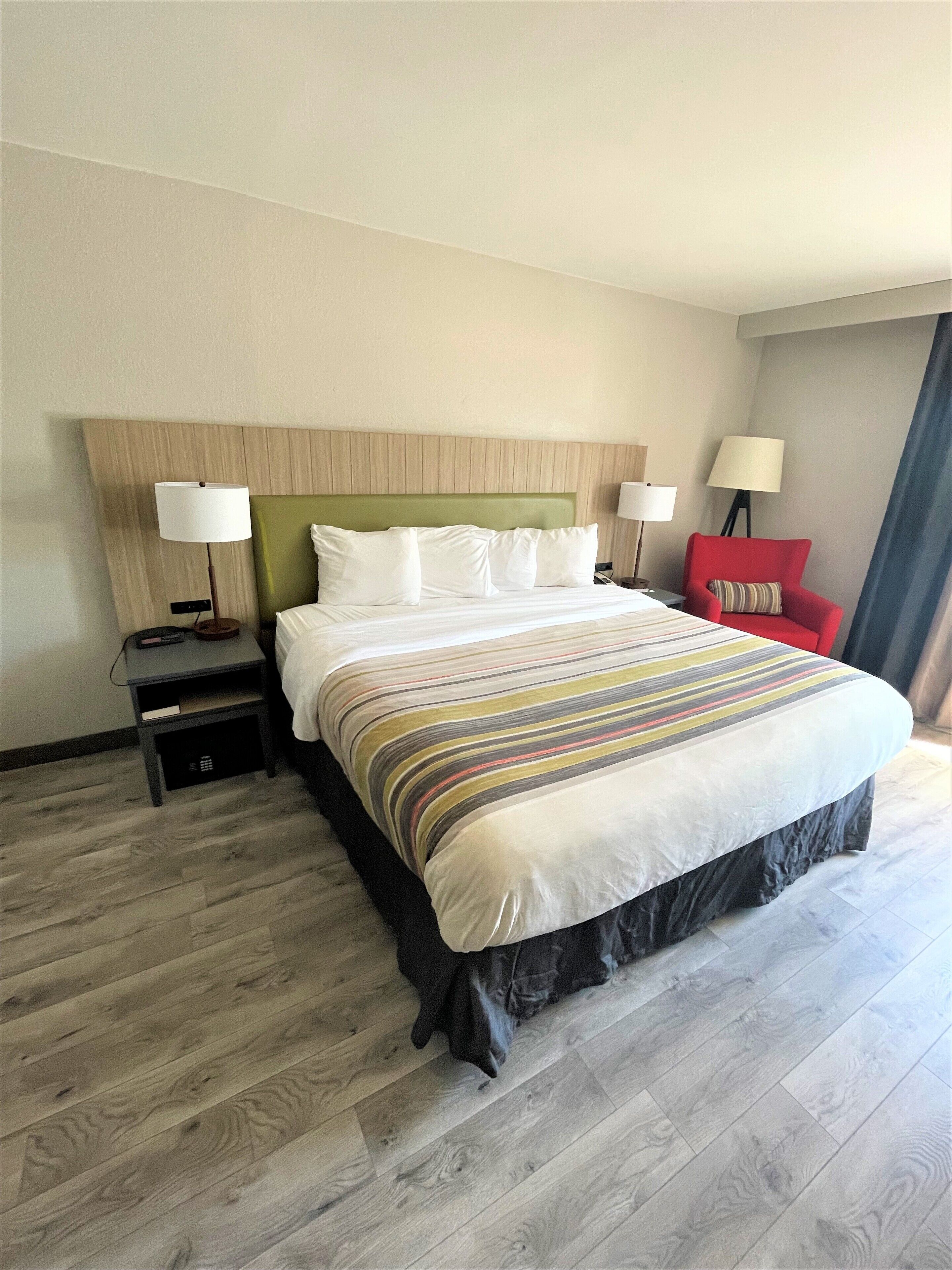 A hotel room with a large bed, two bedside tables, a red armchair, and a window with curtains.