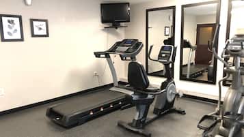 Et fitnessrum med løbebånd, crosstrainer og motionscykel, et fjernsyn på væggen og indrammede billeder.