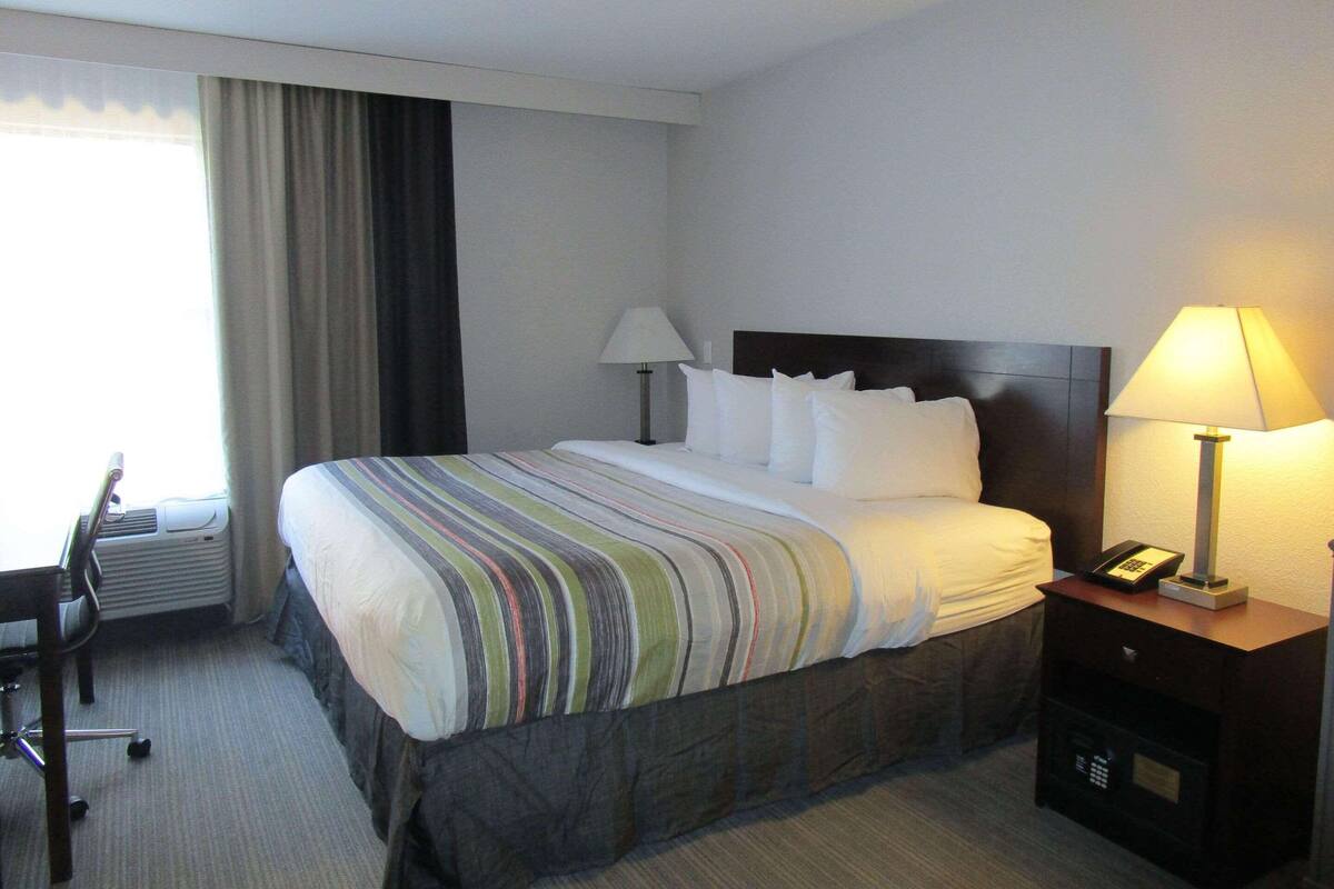 A hotel room with a large bed, two bedside lamps, a desk with a chair, and a telephone on a bedside table.