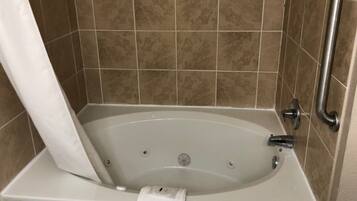 Una bañera con cortina de ducha, un asidero y una toalla blanca en el borde.