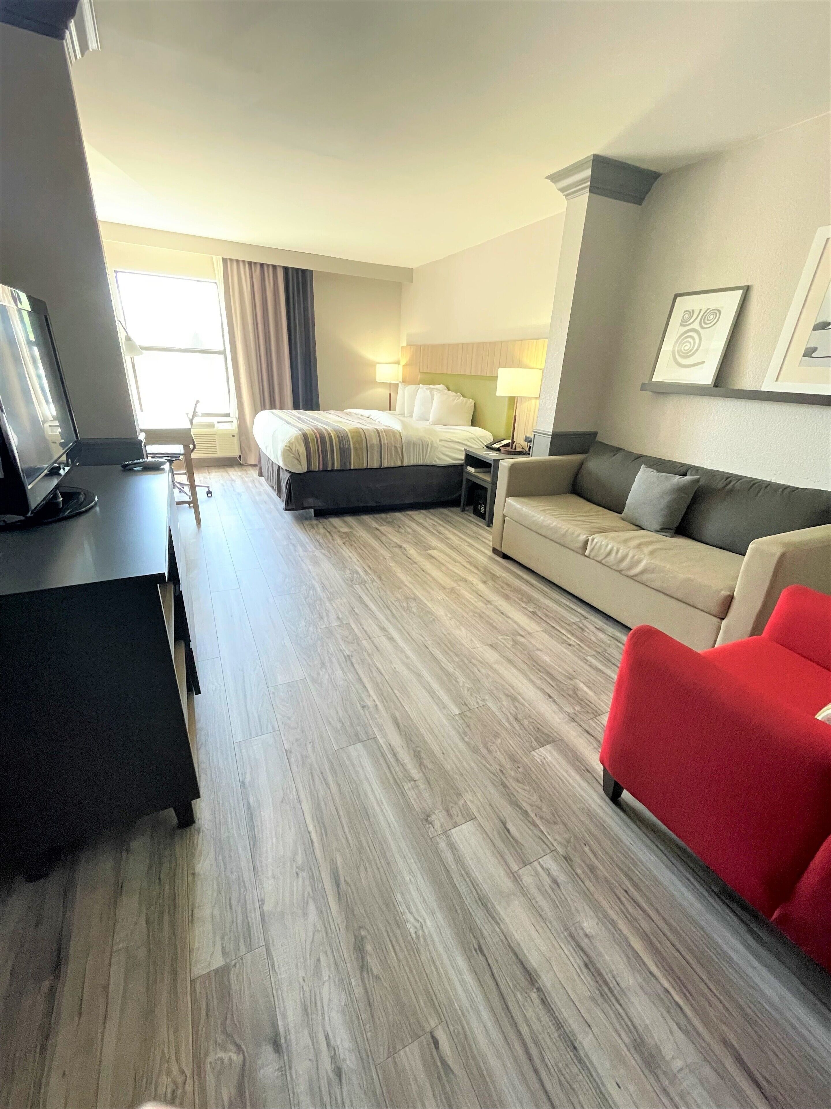 Een hotelkamer met een bed, een bureau met een computer, een rode fauteuil, een bank en een televisie.