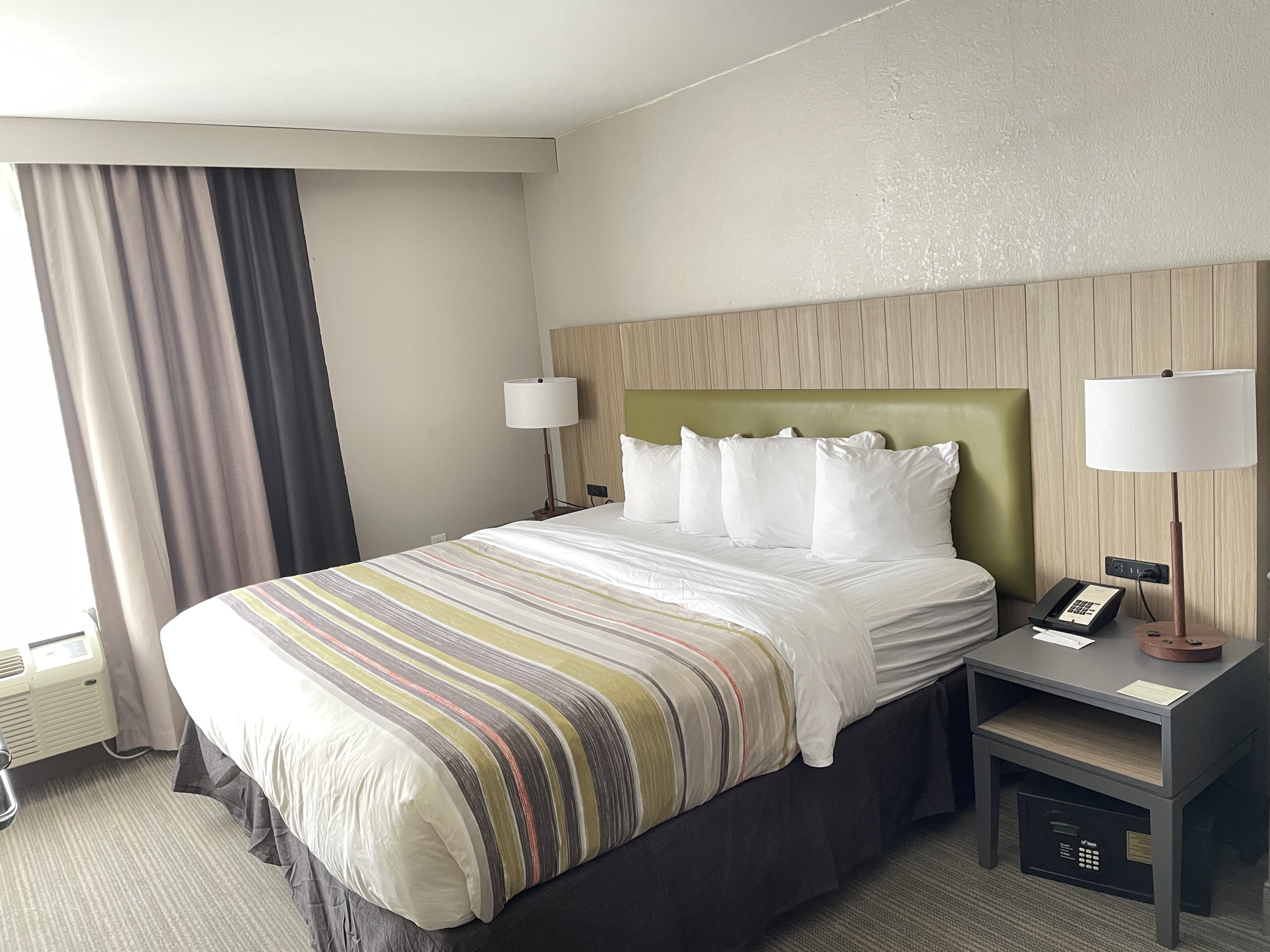 Habitación de hotel con una cama grande, dos mesitas de noche, un cabecero y una ventana con cortinas.