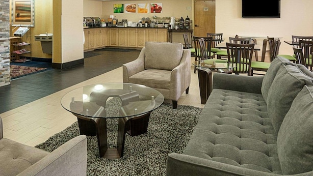 Un hall de hotel con una zona de estar, una estación de café y un televisor montado en la pared.