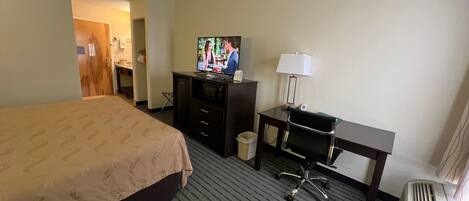 A hotel room with a bed, a desk, a television, a lamp, and a waste bin.