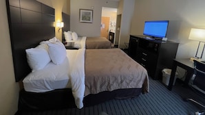 Habitación de hotel con dos camas, un escritorio con computadora, televisión y baño a la vista.