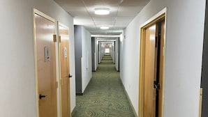 Un largo y estrecho pasillo de hotel con alfombra estampada, puertas de madera e iluminación empotrada en el techo.