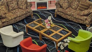 A living room with two floral-patterned sofas, a small white armchair, a red armchair, a green armchair, and a glass coffee table with a floral centerpiece. - Super 8 by Wyndham Staunton (Staunton)
