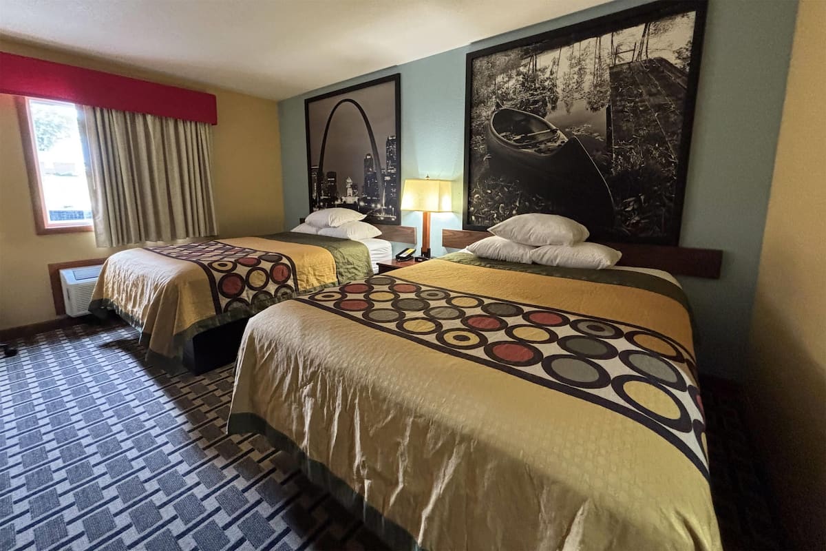 Una habitació d'hotel amb dos llits, un terrapatró, un quadre amb un paisatge urbà i una finestra amb cortines.