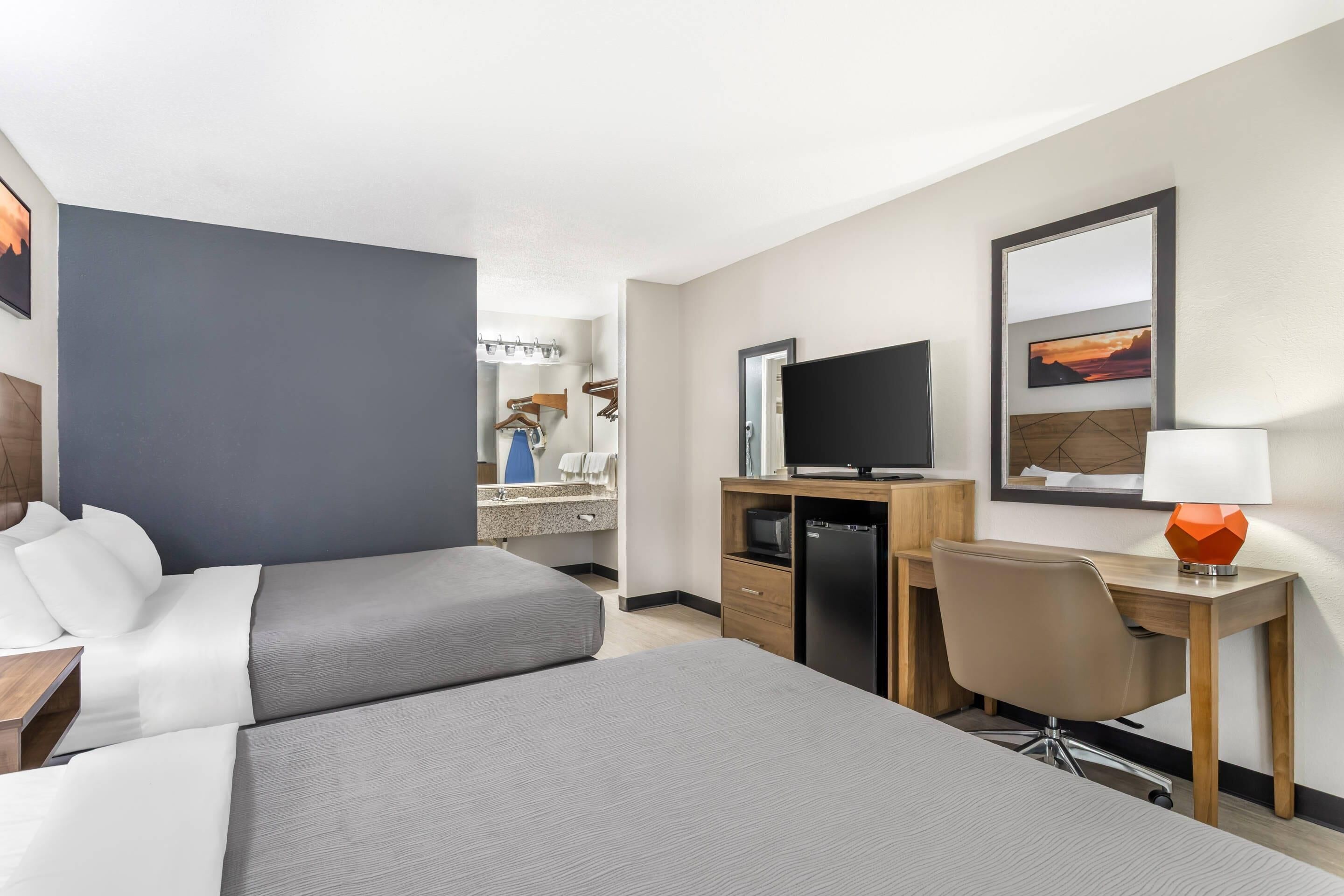 Une chambre d’hôtel avec deux lits, un bureau, une télévision, un miroir et une vue sur la salle de bain.