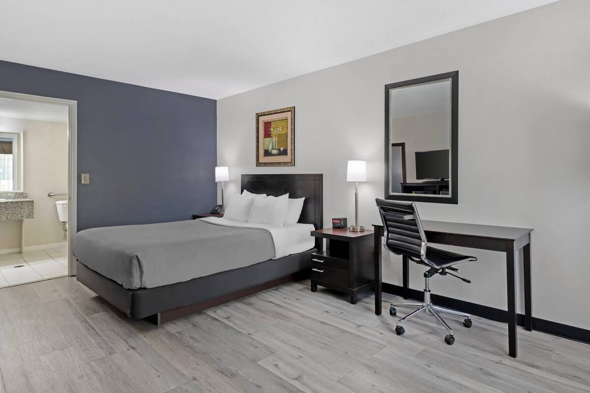 Une chambre d’hôtel avec un lit, un bureau, une chaise, des lampes de chevet et un tableau au mur.