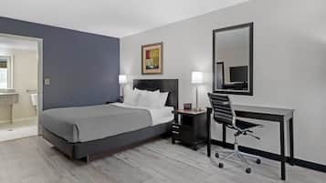 A hotel room with a bed, desk, chair, bedside lamps, and a painting on the wall.