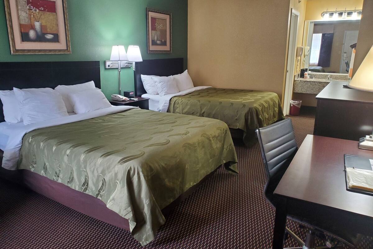 Une chambre d’hôtel avec deux lits, un bureau, une chaise, une lampe et un miroir.
