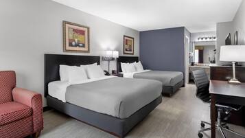 A hotel room with two beds, a desk, a chair, a red armchair, and artwork on the walls.