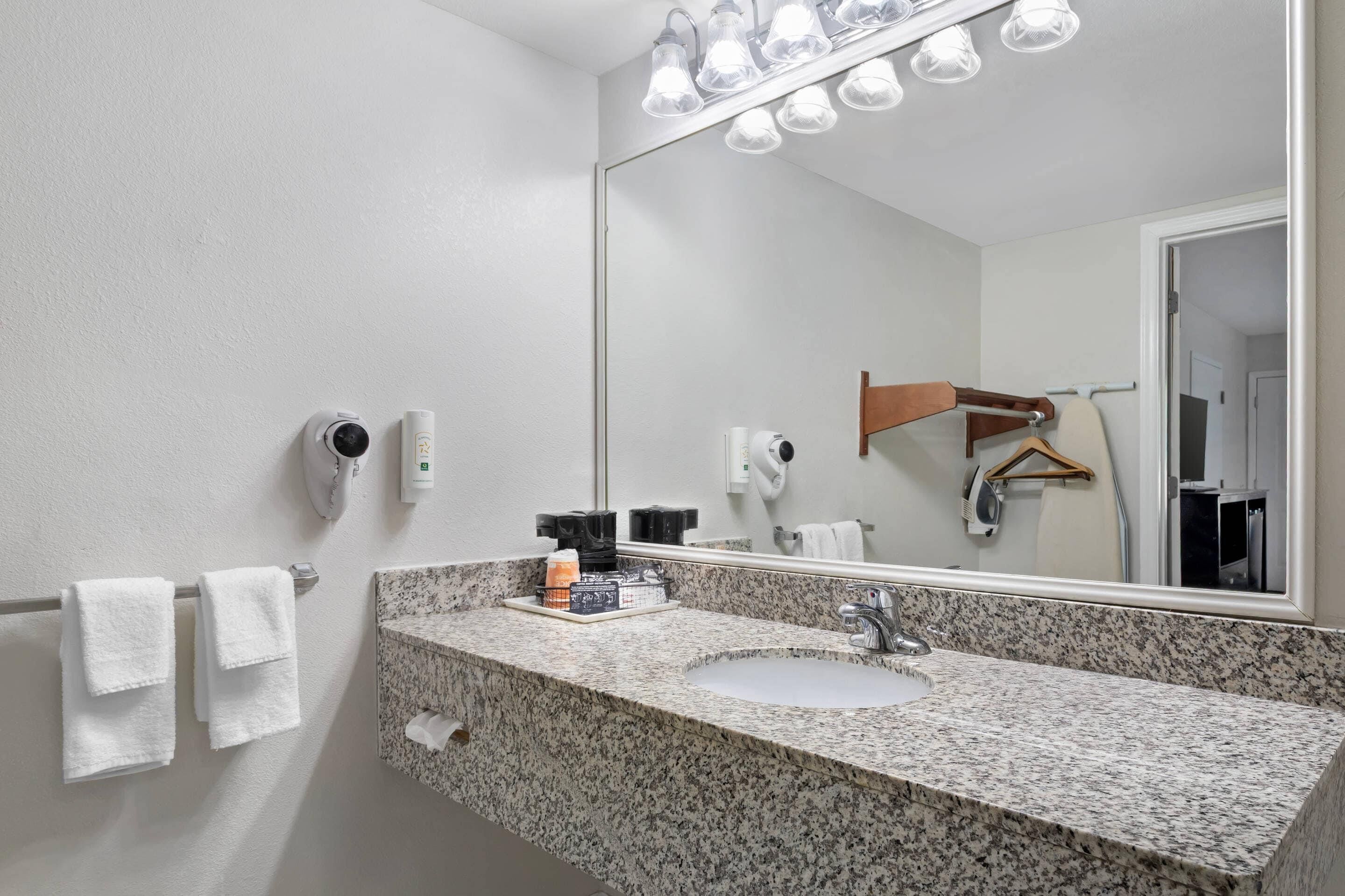 Un bagno con lavabo su piano in granito, uno specchio illuminato, un portascopino e un asciugacapelli.