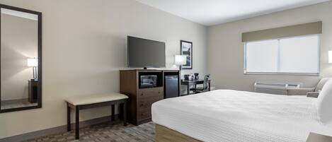 Habitación de hotel con una cama grande, un escritorio, un televisor de pantalla plana, un banco y una ventana con persianas.