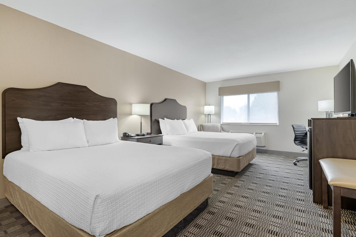 A hotel room with two beds, a desk, a chair, and a TV.