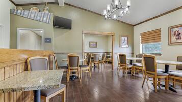 A dining area with wooden tables and chairs, a chandelier, and a television mounted on the wall.