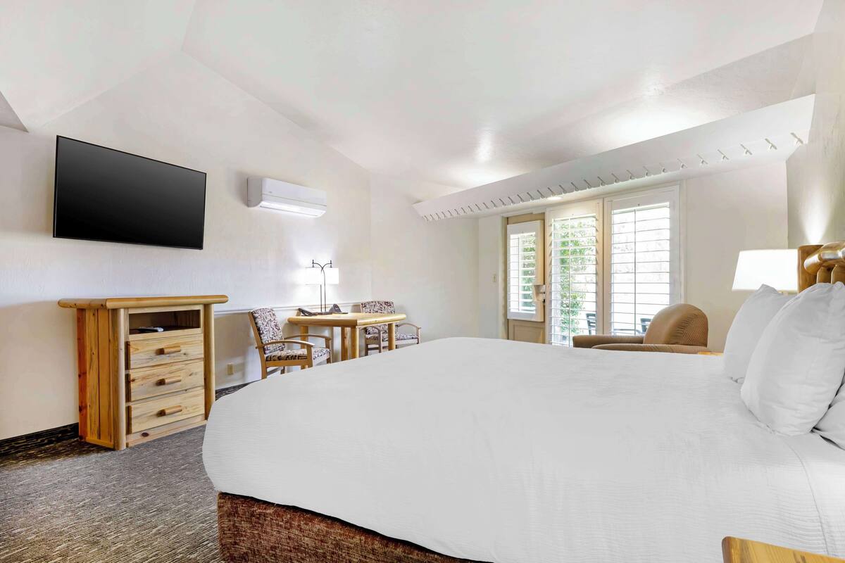 Een hotelkamer met een groot bed, een bureau met stoel, een flatscreen televisie aan de wand en een raam met zonwering.