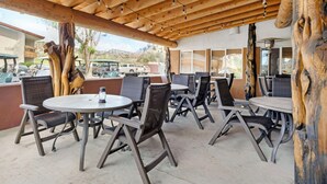 Een buitenterras met ronde tafels en stoelen, houten balken erboven en grote boomstammen verwerkt in het ontwerp.