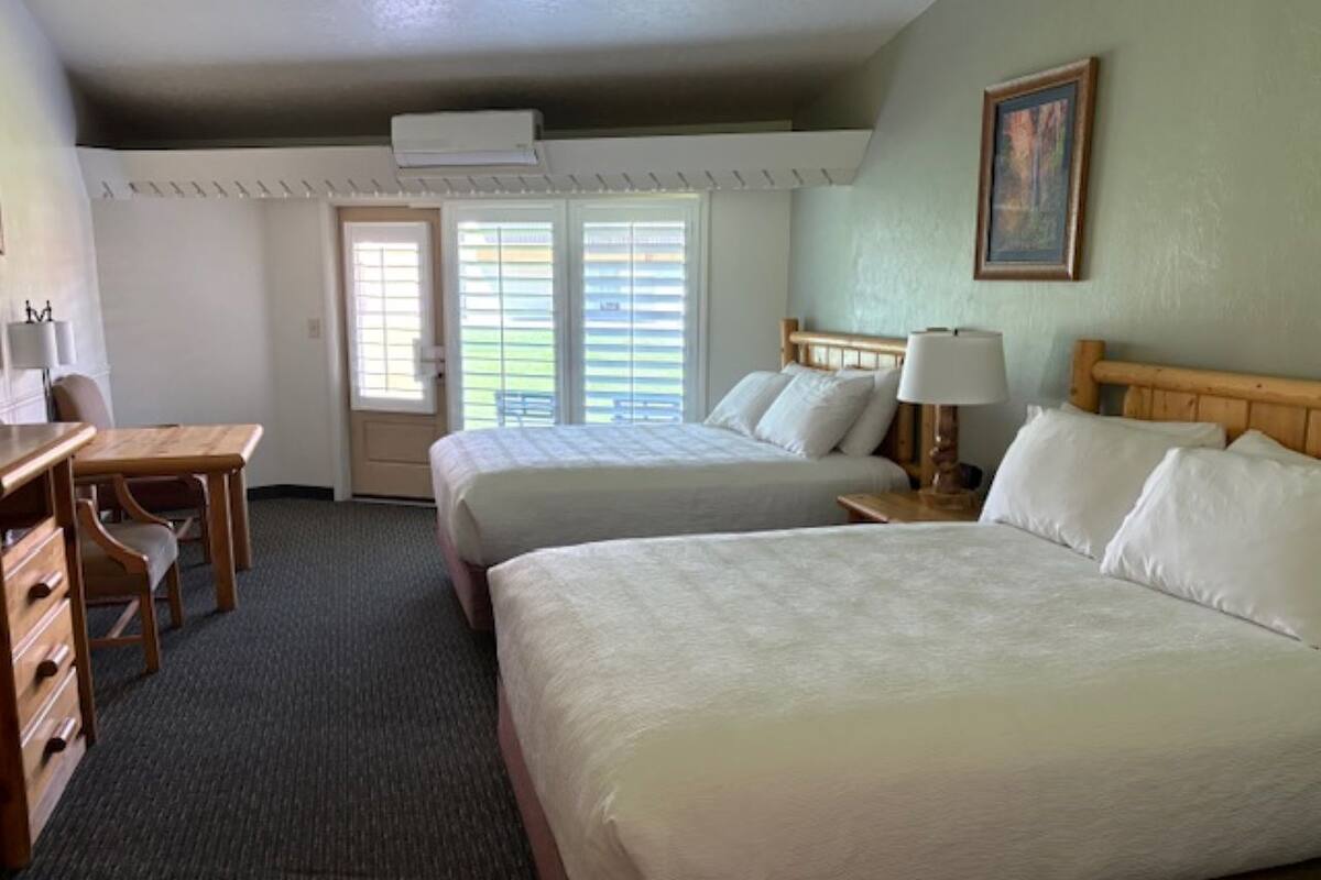 Hotelkamer met twee bedden, een bureau en een stoel. Een deur met een raam en een airconditioning op de muur.