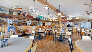 Een restaurant met houten vloeren, meerdere eettafels en zithoeken, plafondventilatoren en diverse borden aan de muren.