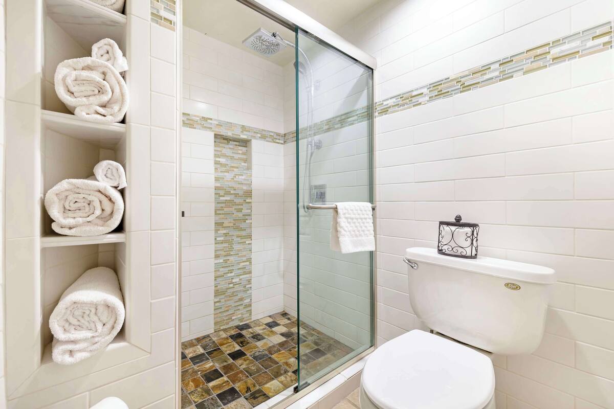 Een badkamer met een douche met glazen wand, witte betegelde wanden en een toilet met een witte zitting.