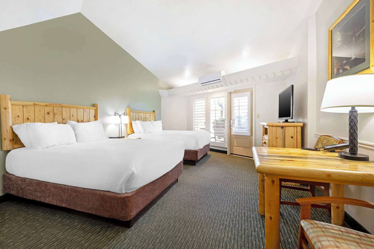 Een hotelkamer met twee bedden, een houten hoofdeinde, een televisie, een tafel met lamp en een raam met jaloezieën.