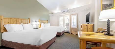 A hotel room with two beds, a wooden headboard, a television, a table with a lamp, and a window with blinds.
