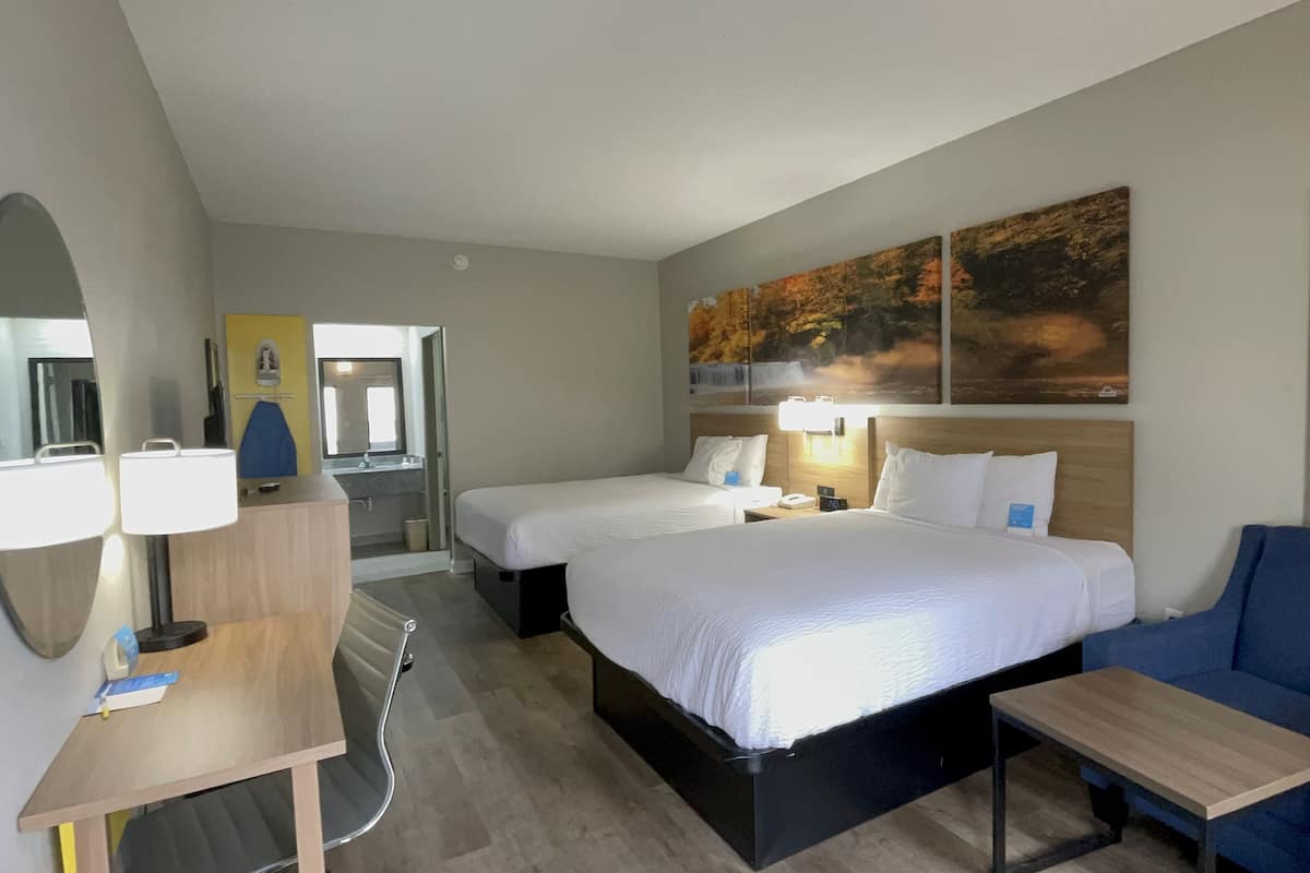 A hotel room with two beds, a desk, a chair, and a large mirror.