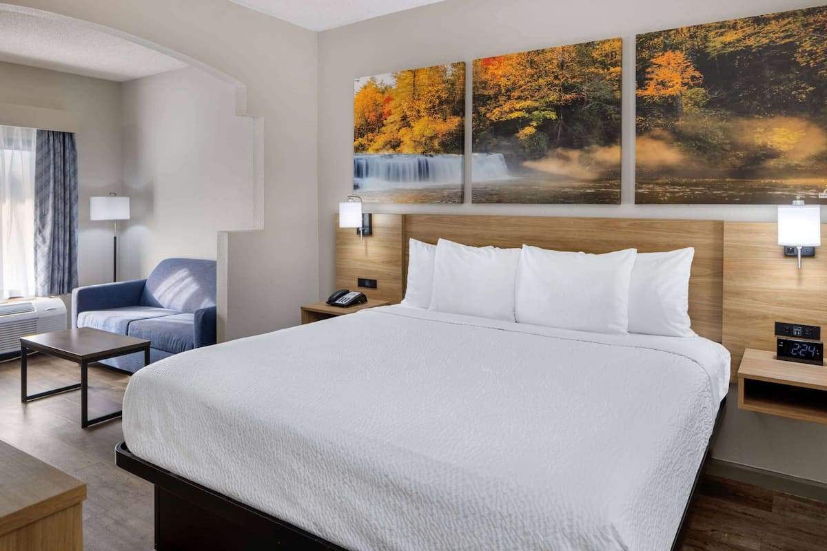 A hotel room with a large bed, a desk, a chair, a nightstand with a phone, and a wall-mounted clock.