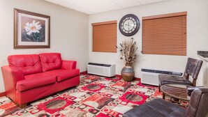 Ein Wohnzimmer mit einem roten Sofa, einem braunen Ledersessel, einem gemusterten Teppich, einer Wanduhr und einem gerahmten Blumenbild.