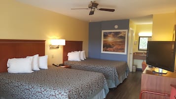 Quarto de hotel com duas camas, um ventilador de teto, uma luminária de parede, um quadro, uma escrivaninha com telefone e uma televisão.