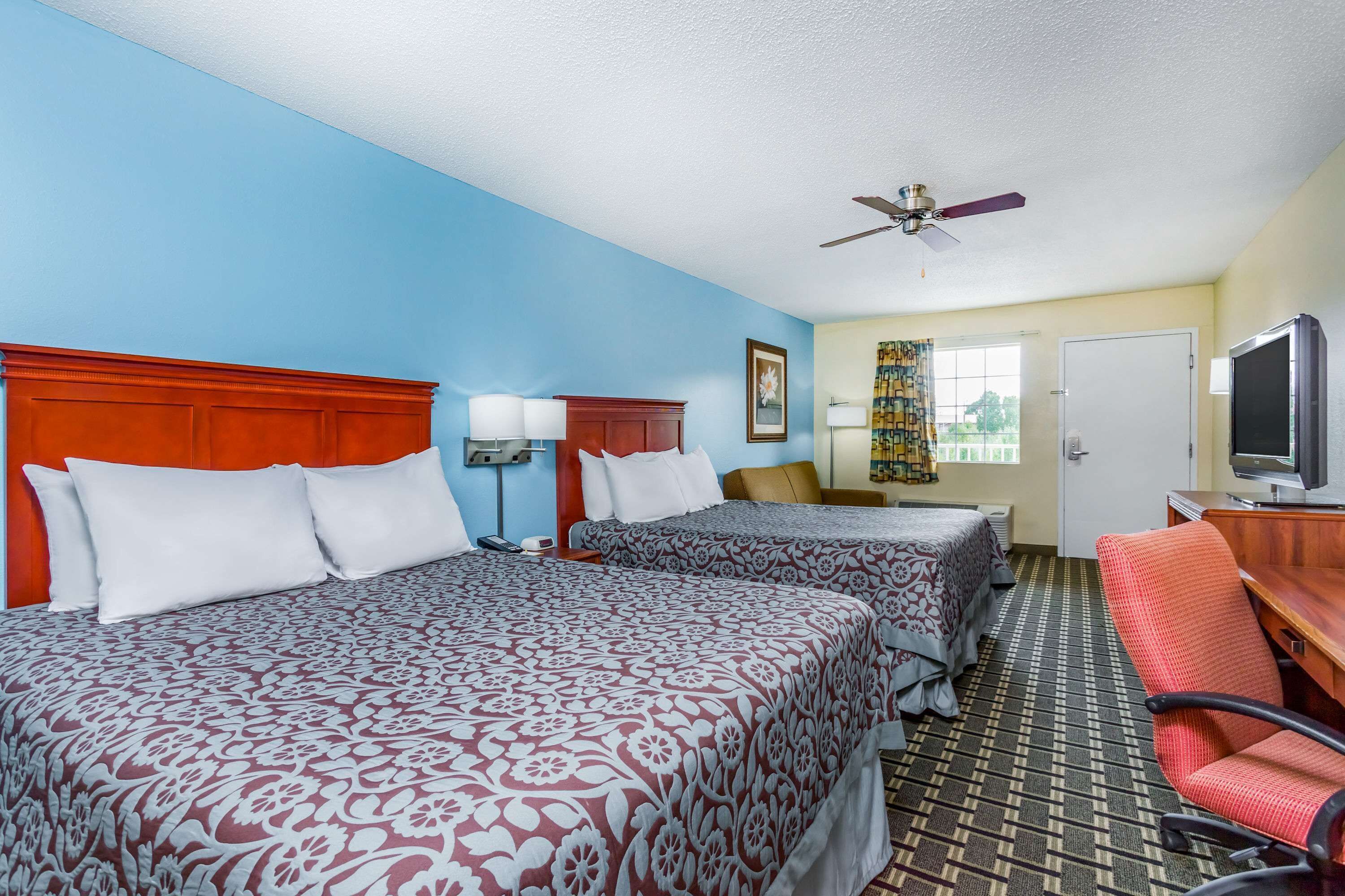 A hotel room with two beds, a ceiling fan, a television, and a desk.