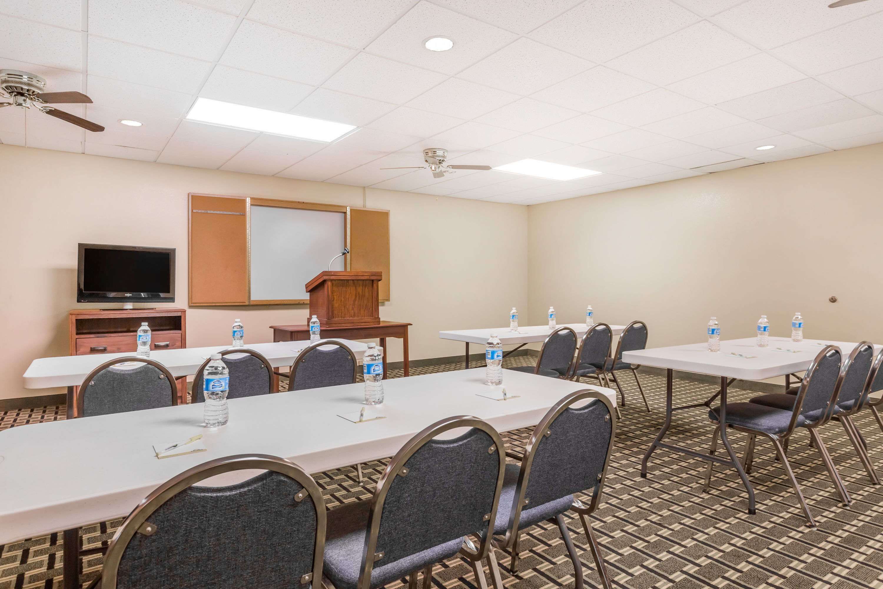 A conference room with white tables, chairs, and a TV.