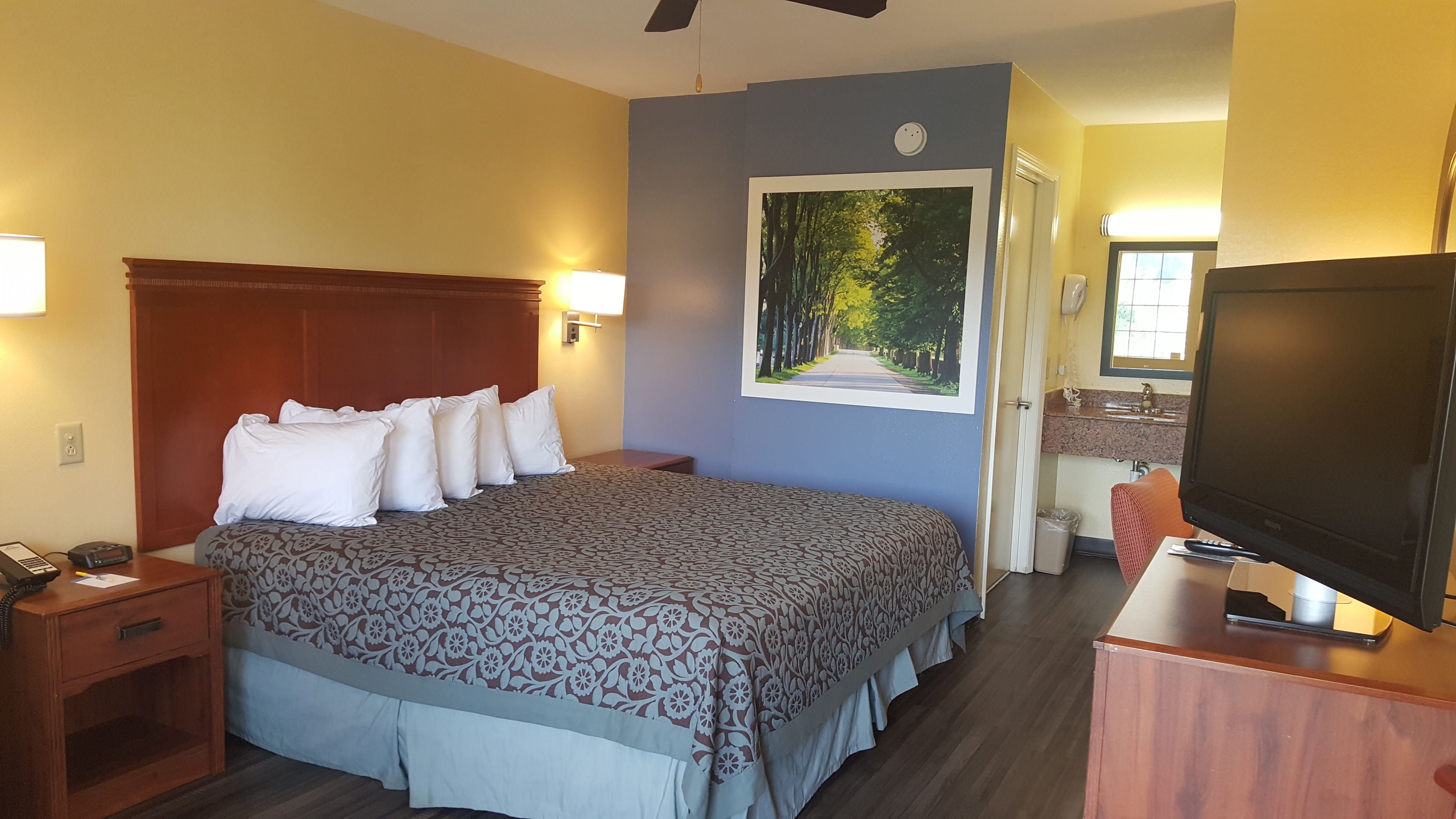 Ein Hotelzimmer mit einem großen Bett, einem Fernseher, einem Schreibtisch und einem durch eine offene Tür einsehbaren Badezimmer.