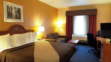 Habitació d'hotel amb llit, escriptori amb cadira, televisió i finestra amb cortines.