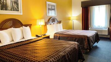 A hotel room with two beds, a headboard, a nightstand, a lamp, a framed picture on the wall, and an air conditioning unit.