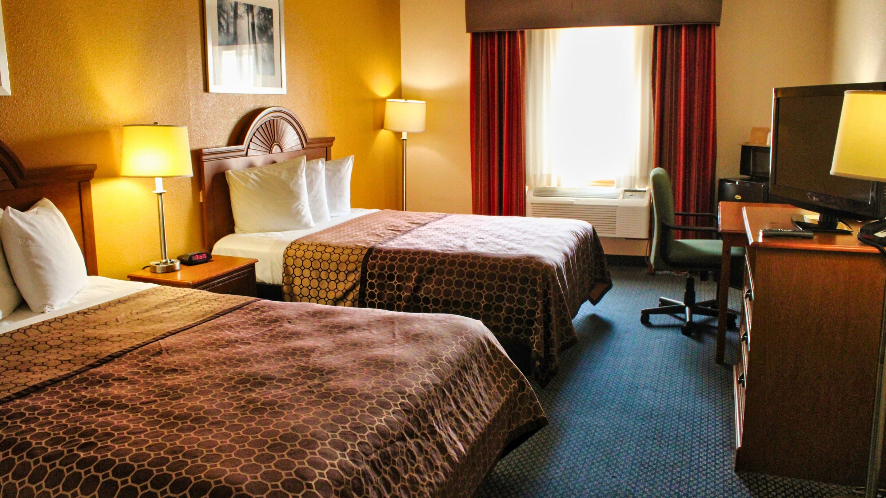 Habitación de hotel con dos camas, un escritorio con ordenador, una silla y una ventana con cortinas.