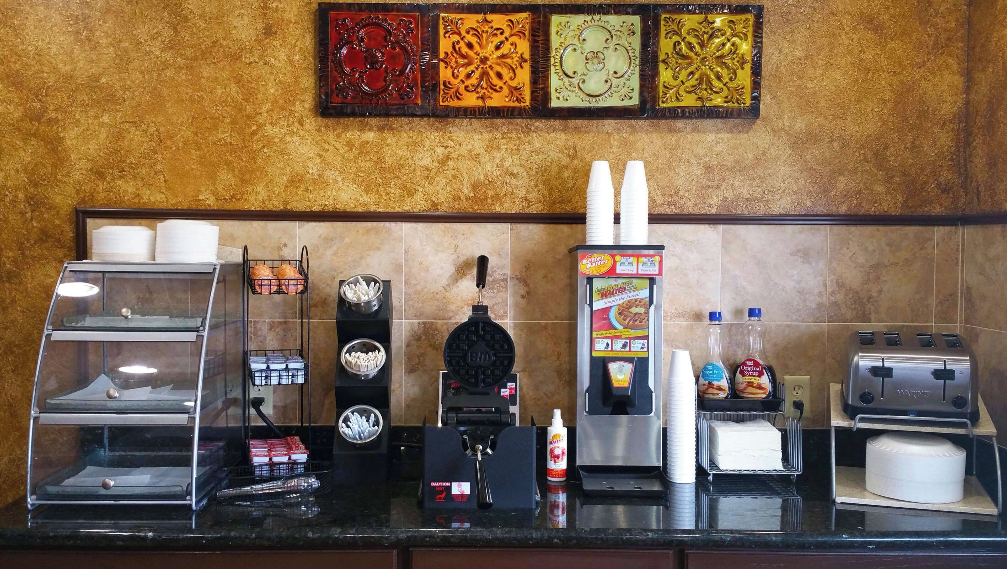 A kitchen counter with a waffle maker, coffee machine, and various condiments.